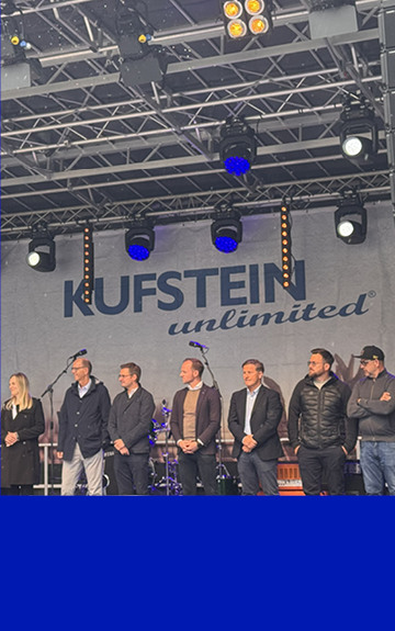 Mehrere Personen stehen bei der offiziellen Eröffnung von Kufstein Unlimited auf einer Bühne vor einem großen Banner mit der Aufschrift „Kufstein unlimited“. Fotocredit: Volksbank